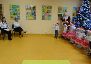 Grupa dzieci śpiewa piosenkę. Pani dyrektor Maria Królikowska i pani Ewelina Cicha przyglądają się dzieciom.